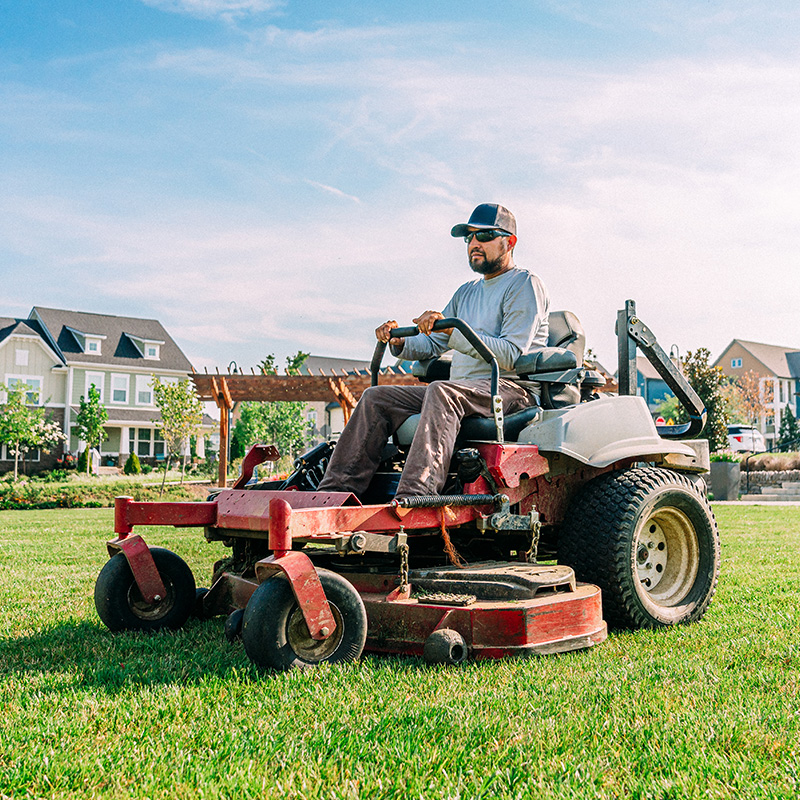 Low Angle View of a Man Using a Riding Lawnmower near an Apartment Complex