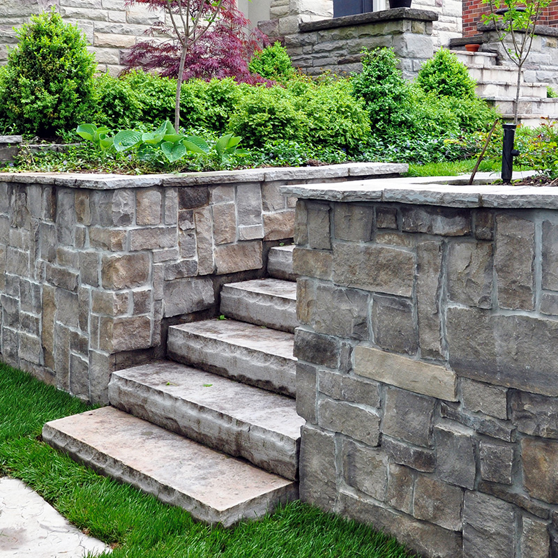 Luxury landscaping shows natural stone steps, a retaining wall with coping, and oversized flagstone stepping stones.